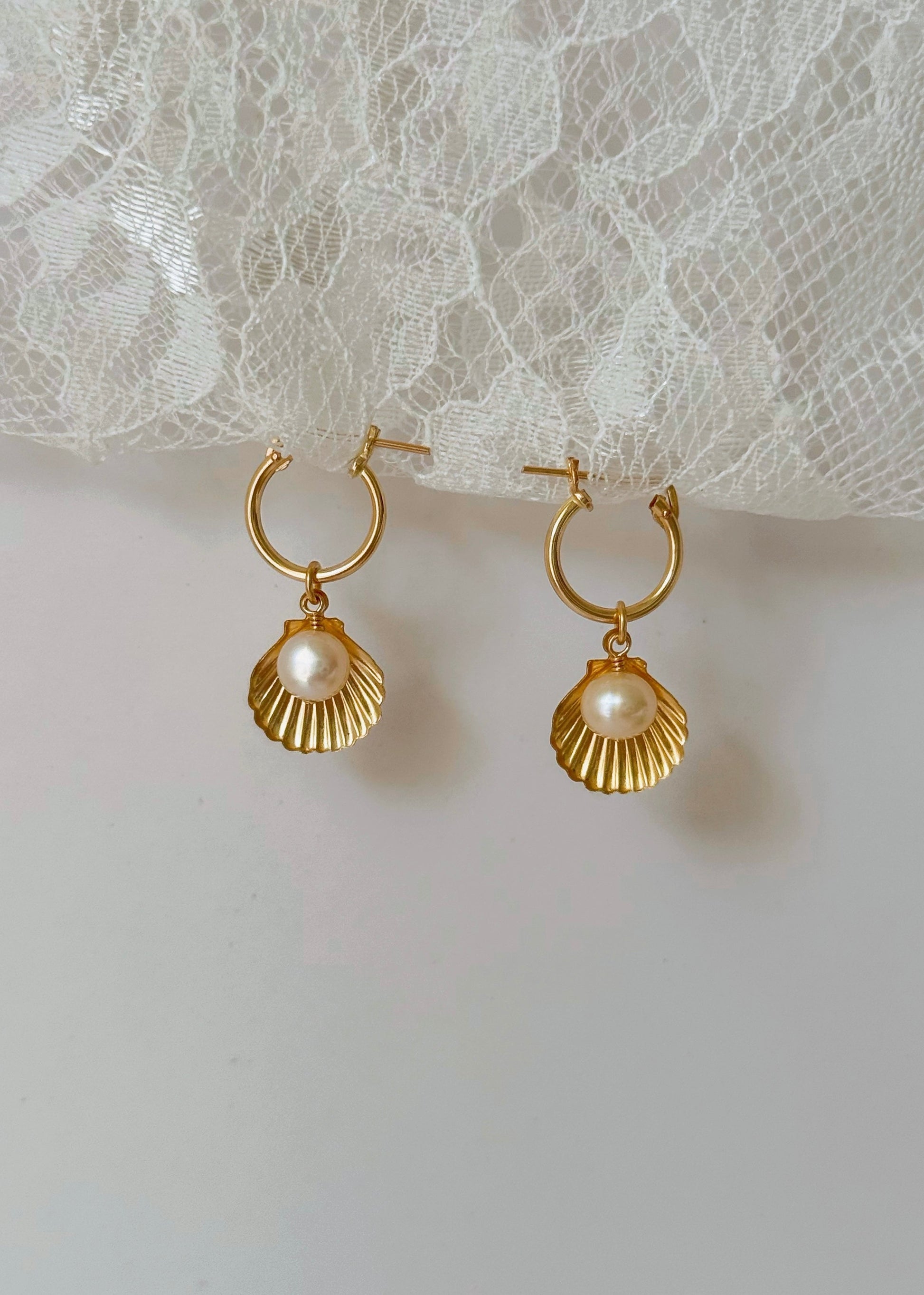 Gold hoop earrings with pearl drops on a lace background